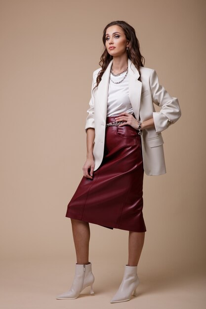 Woman in white leather jacket red long skirt boots accessories on beige background