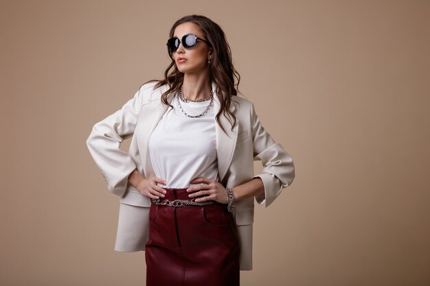 Woman in white leather jacket red long skirt boots accessories sunglasses on beige background