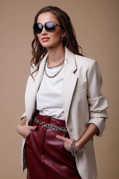 Woman in white leather jacket red long skirt boots accessories sunglasses on beige background