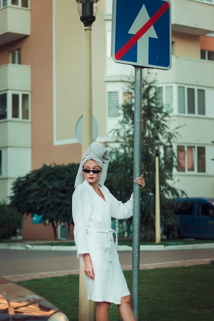 A woman in a white outfit is standing on a street corner with a sign that says no to go