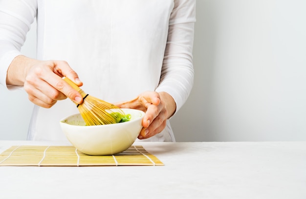 Woman in white prepare Japanese green Matcha tea by whipping it in a bowl 