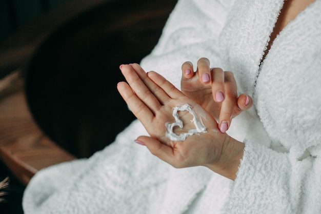 A woman in a white robe on her hand painted a heart with white cream