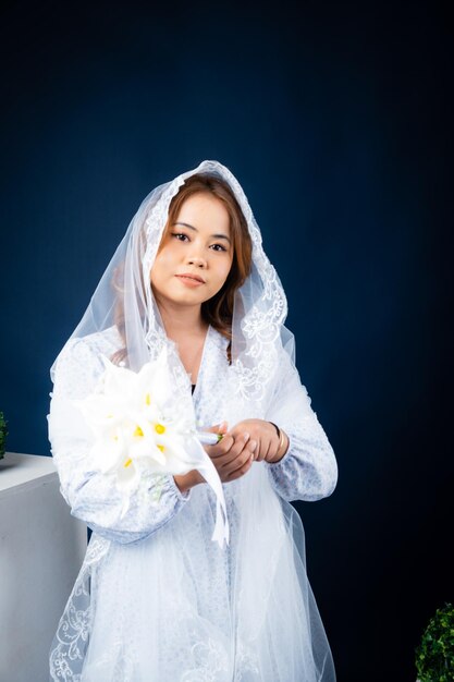 A woman in a white robe holds a bunch of flowers.
