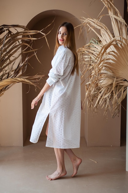 A woman in a white robe stands in front of a palm tree.