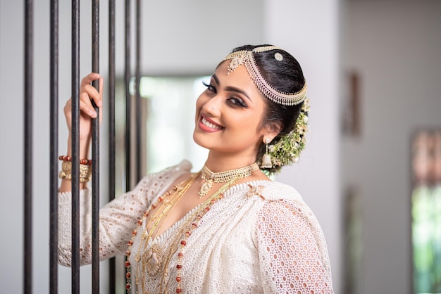 A woman in a white saree smiles at the camera.