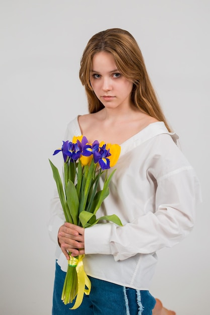 흰 셔츠와 청바지를 입은 한 여성이 앉아서 튤립과 붓꽃 꽃다발을 들고 있습니다.