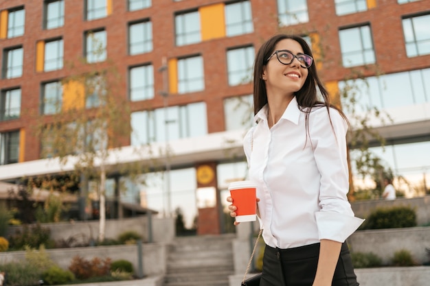 Woman in white shirt holding a coffee to go