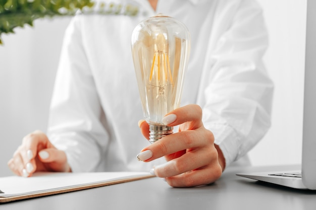 Woman in white shirt holding light bulb in hand