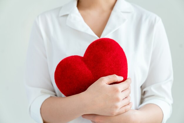 Woman in a white shirt holding red hearts on gray background.