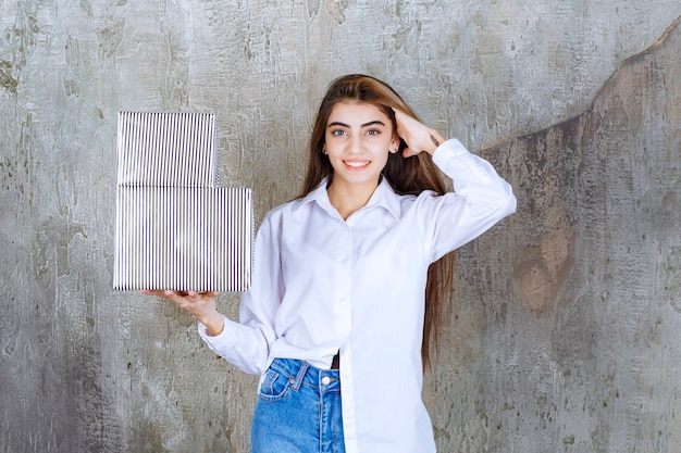 Photo woman in white shirt holding silver gift boxes and feeling seductive.