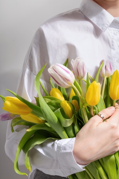 白いシャツを着た女性は彼女の手で黄色とピンクのチューリップの花束を持っています