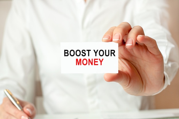 A woman in a white shirt holds a piece of paper with the text: BOOST YOUR MONEY. Business concept for companies.