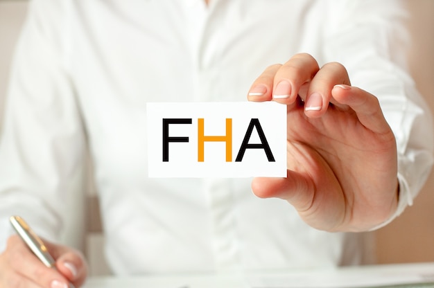 A woman in a white shirt holds a piece of paper with the text: FHA. Business concept for companies. FHA - short for finance houses association.