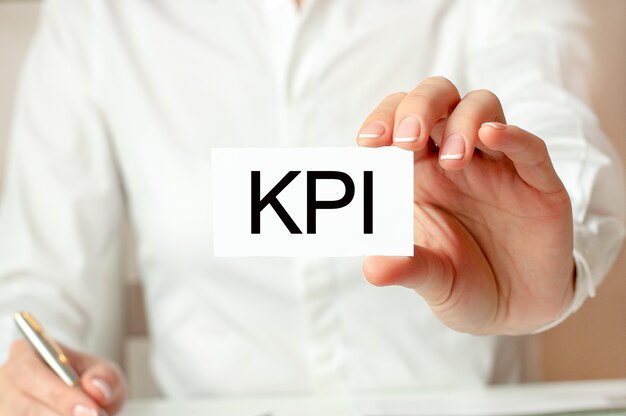A woman in a white shirt holds a piece of paper with the text KPI.