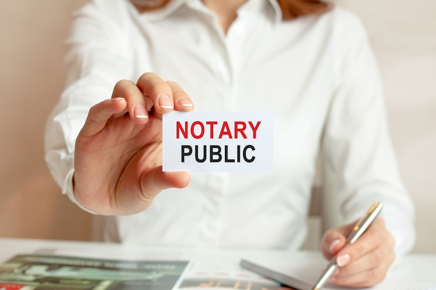 A woman in a white shirt holds a piece of paper with the text:
notary public. business concept for companies