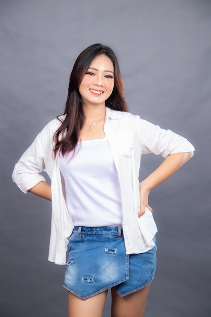 A woman in a white shirt and jeans stands in front of a grey background casual female promo fashion