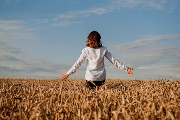 A woman in white shirt in rye field. View from the back. The concept of harmony