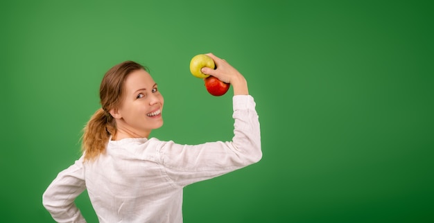 白いシャツを着た女性は、緑の背景にリンゴの力を示しています。ダイエット、健康食品、菜食主義の概念。