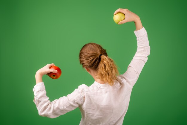 Женщина в белой рубашке демонстрирует силу яблок на зеленом фоне. Понятие диеты, здорового питания, вегетарианства.