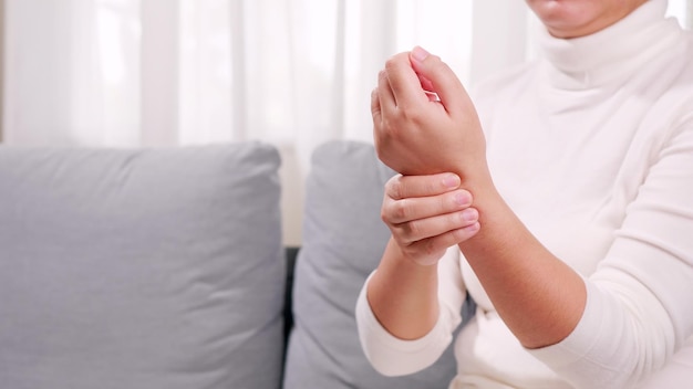 A woman in a white shirt sits on the sofa and massages her arms and wrists. To relax and to relieve pain. Health care concept