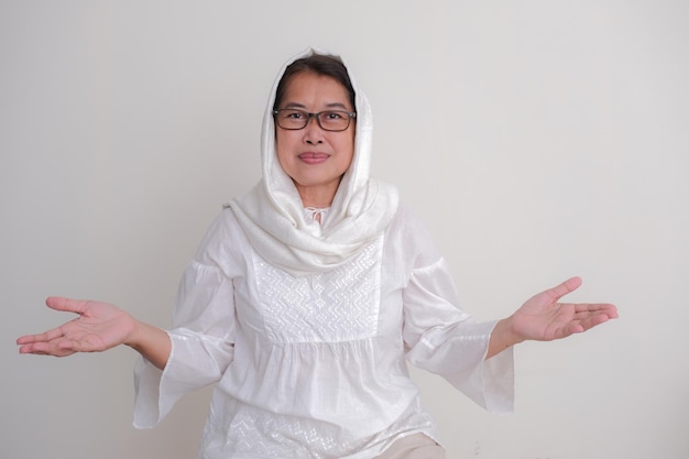 A woman in a white shirt with a scarf on her head and glasses with her hands open.