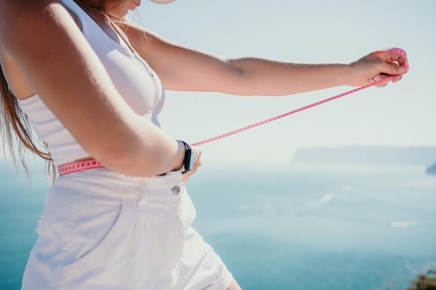 Woman in white shorts holds in her hands pink measuring tape on her waist near the azure sea concept