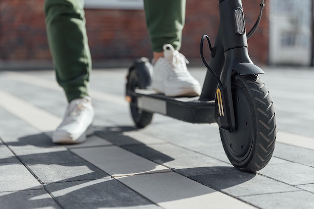 Woman in white sneakers is standing on electric scooter