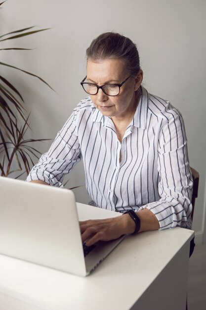 Woman in a white striped shirt aged sits at a computer at home with glasses