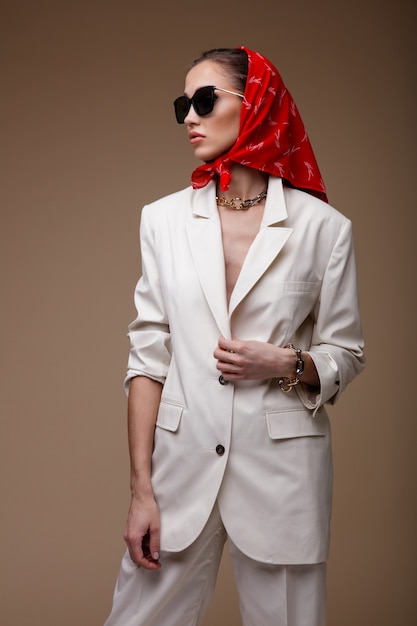 Woman in white suit jacket pants shoes red scarf  sunglasses accessories on beige background