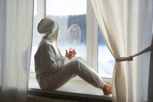 A woman in a white suit sits at a winter window