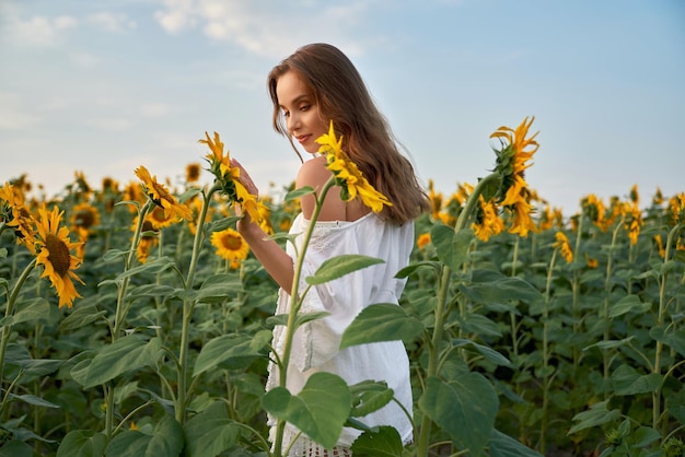 Woman in white summer dress standing on field with sunflower