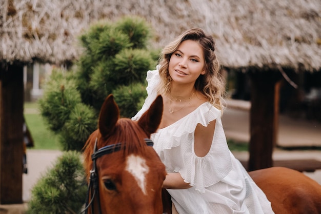 Женщина в белом сарафане верхом на лошади возле фермы