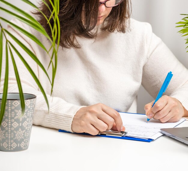 Photo woman in a white sweater and glasses signs documents on the table. conclusion of a deal, contract