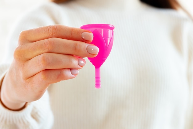 Woman in white sweater holding pink menstrual cup in hands close up photo