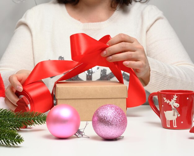 Woman in a white sweater sits at the table and wraps gifts for Christmas Preparing for the holidays