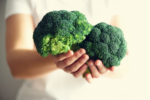 Woman in white T-shirt holding broccoli in hands. 