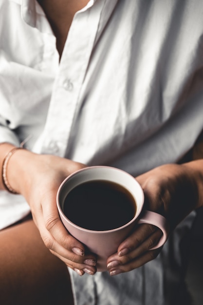 Woman in a white t-shirt holds morning coffee in a pink ceramic cup. Manicure. Front view