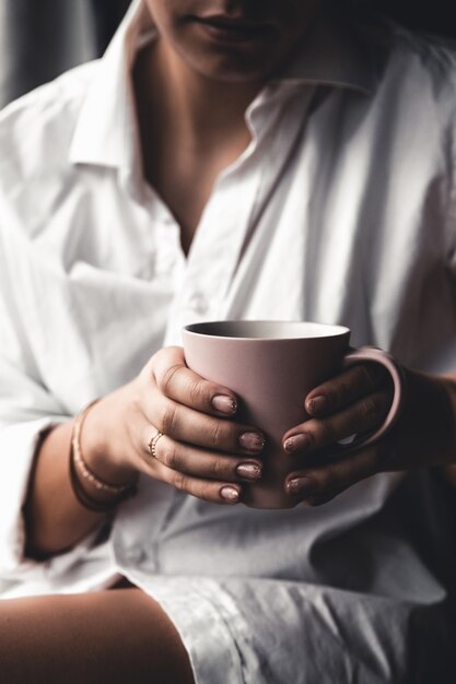 Woman in a white t-shirt holds morning coffee in a pink ceramic cup.