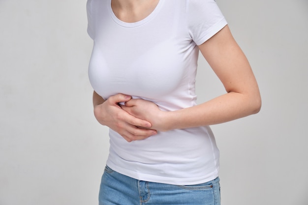 A woman in a white T-shirt massages her stomach with her hands. Belly pain. The concept of poisoning. Muscle spasm.