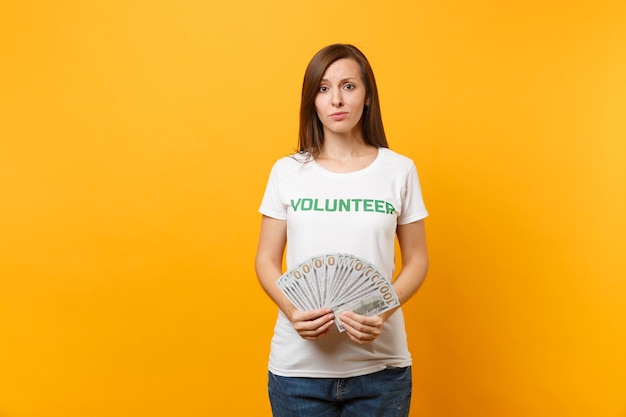 Woman in white t-shirt with written inscription green title volunteer hold lots dollars banknotes, cash money isolated on yellow background. Voluntary free assistance help, charity grace work concept.