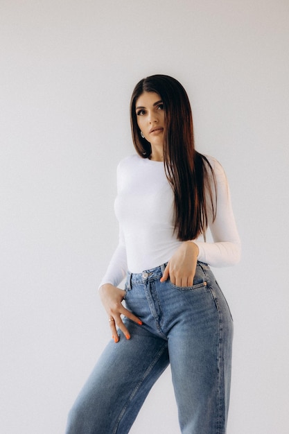 a woman in a white top and jeans stands in front of a white background