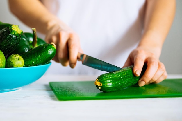 Woman in white tshirt cut cucumber on green board healthy food concept