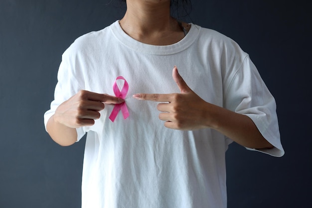 woman in white tshirt holds and finger pointing pink breast cancer awareness ribbon