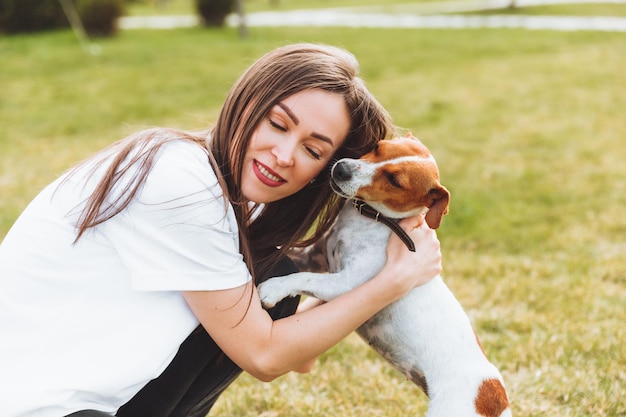 A woman in a white Tshirt and jeans hugs her Jack Russell Terrier dog in nature in the park Loyal best friends since childhood Lifestyle