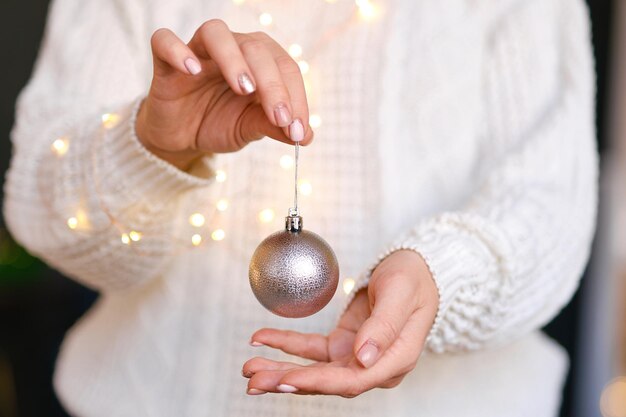 手におもちゃの装飾的なボールを保持している白い暖かいウールのセーターの女性