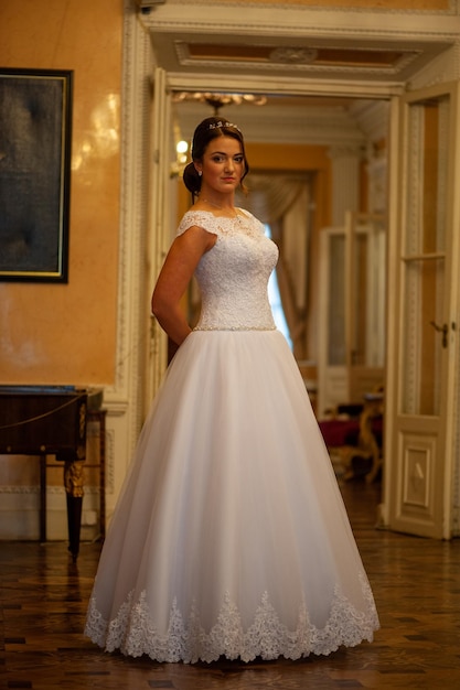 A woman in a white wedding dress stands in a room with a painting on the wall.