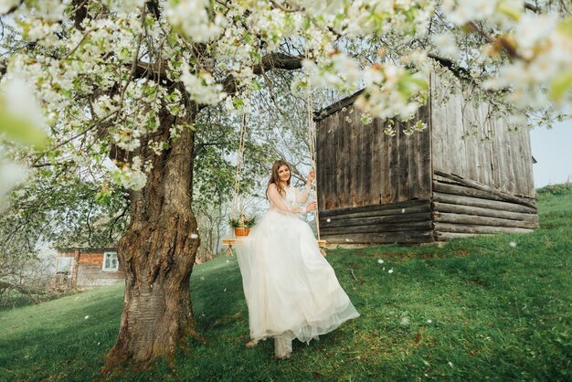 スイング花の咲く木の背景に白いウェディングドレスの女性。春の屋外での結婚式の花嫁。女性の肖像画