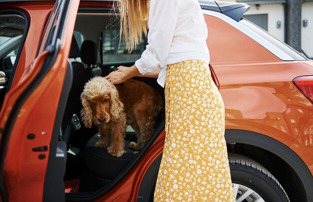 Photo woman in white and yellow clothes is with her dog near the car.