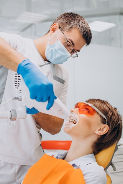 Woman whitening teeth at dentistry with special equipment