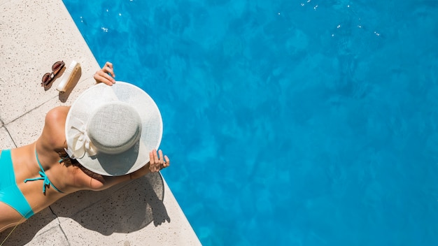 Photo woman in wide-brimmed hat lying on pool border